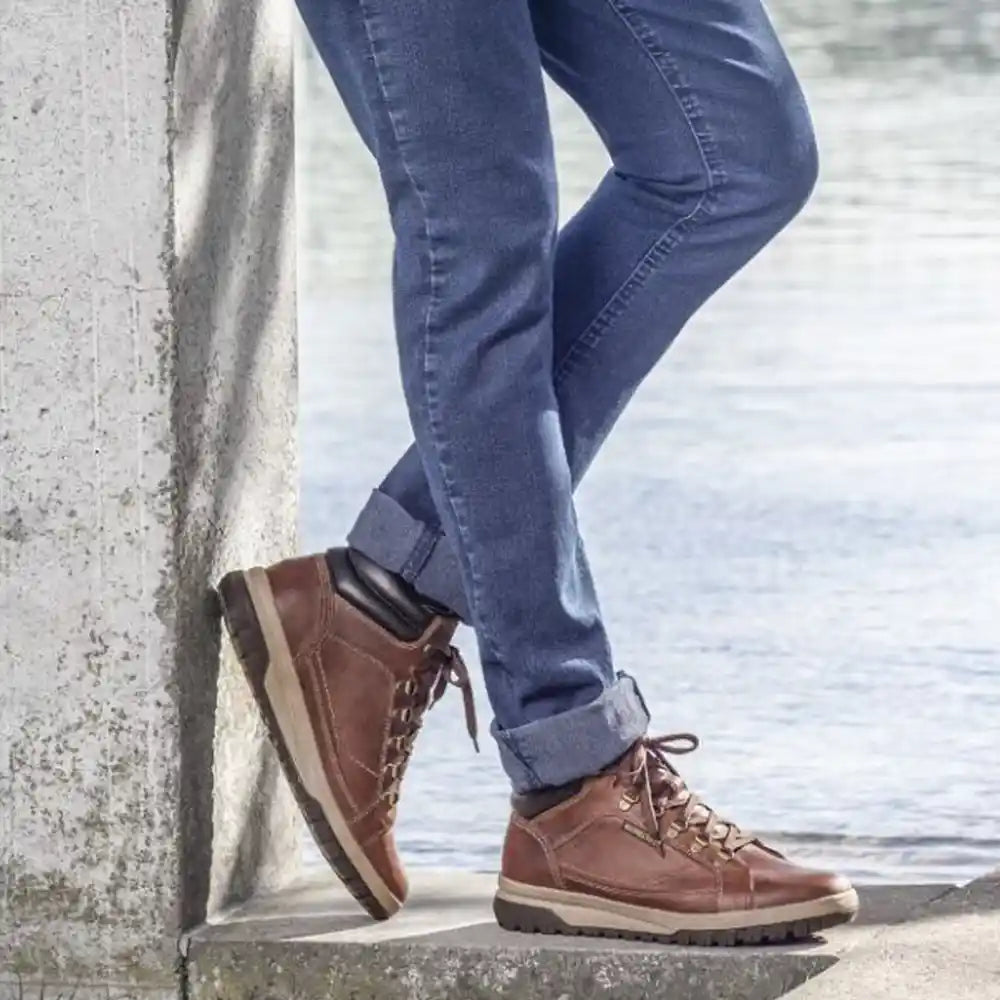 Brown boots and blue jeans against a concrete wall.