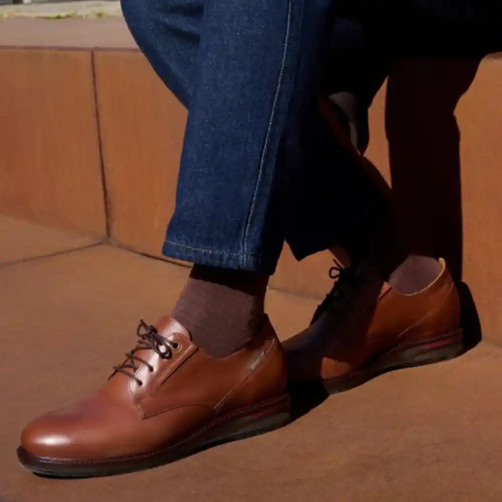 Brown leather shoes worn with blue jeans on a brown surface