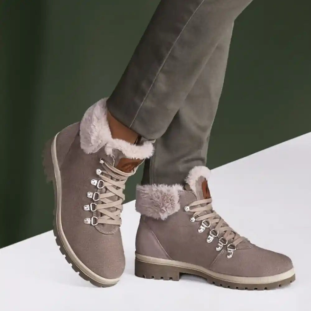Gray winter boots with fur trim worn by a person on a white surface with a green background