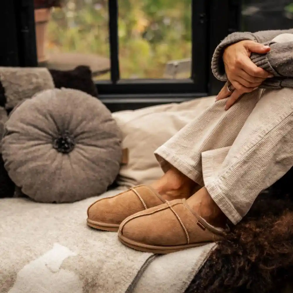 Person wearing tan slippers on a cozy couch with a blurred outdoor background