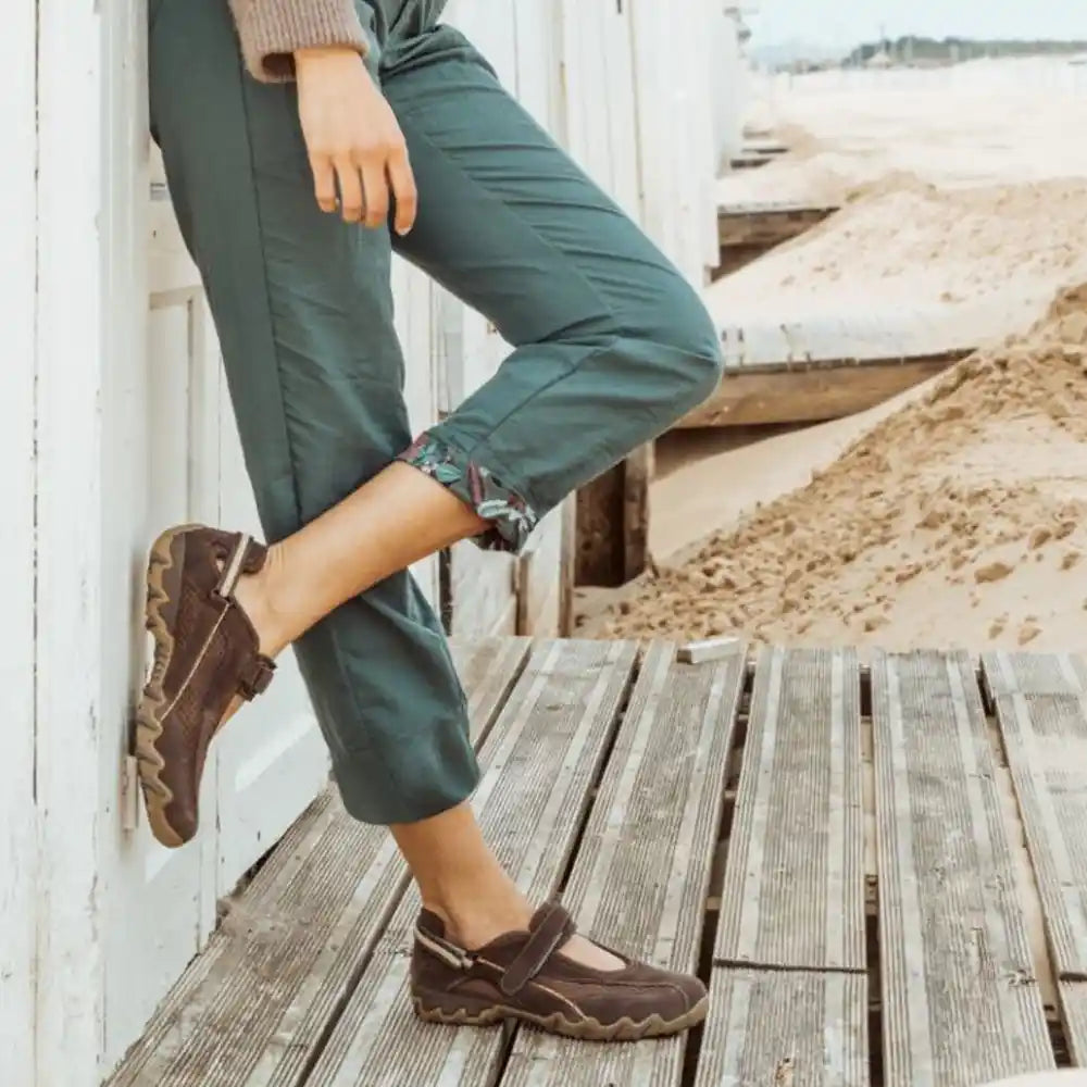 Person wearing green pants and brown shoes on a wooden deck with a beach background